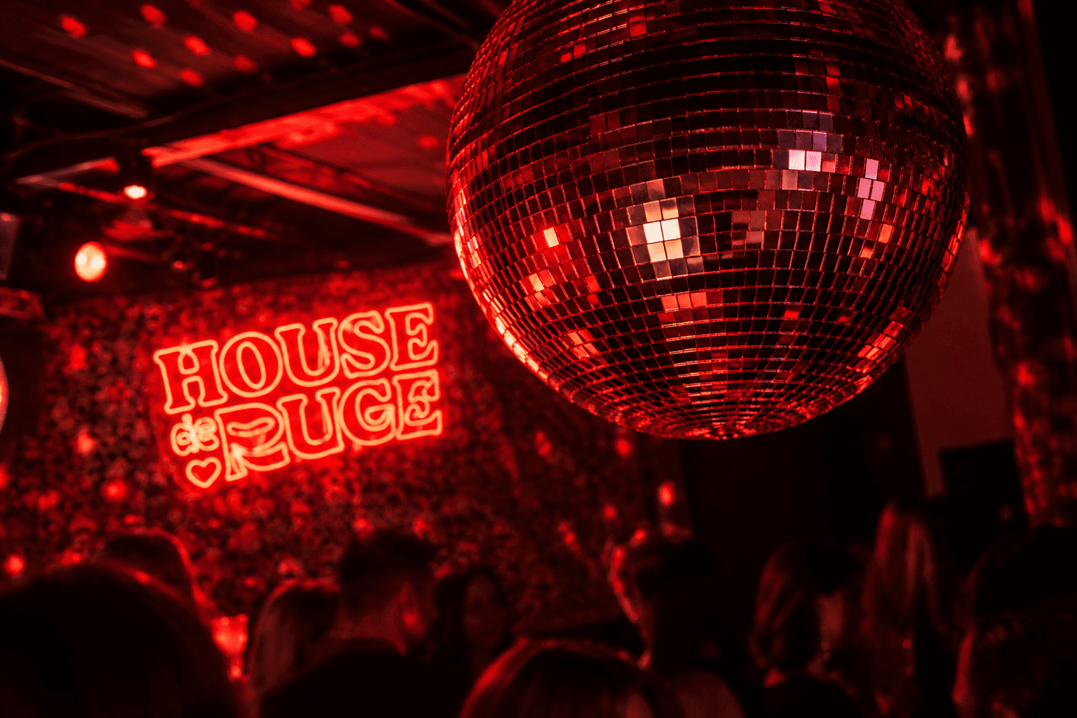 Discokugel im roten Licht neben der Neonschrift „House de Rouge“